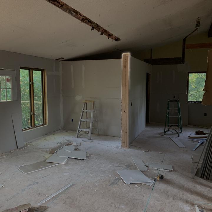 A half-finished room with drywall on the walls, an open ceiling, two ladders and debris on the subfloor, photographed July 10, 2024